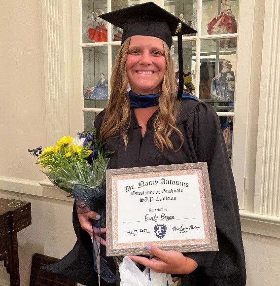 Emily Bryan dressed in cap and gown holds flowers and her award for Outstanding Clinician.